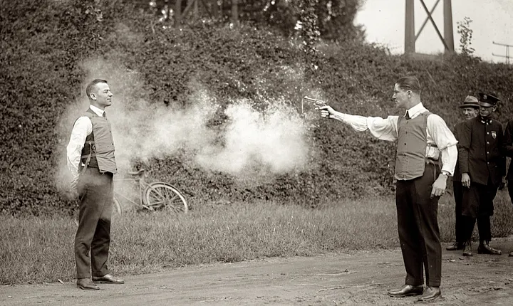 A man shooting another, wearing a very rudimentary bulletproof vest